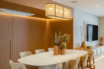 Sala de jantar com mesa oval, painel em madeira e luminária pendente — reforma residencial